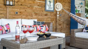 A cozy room with a wicker sofa, a dining table with a bottle of wine and glasses, and a hammock. - Villa in Escales With Private Pool (Escales)