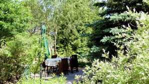Zona d'exterior per dinar amb taula i cadires, envoltada de vegetació i arbres frondosos.