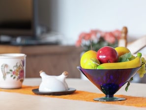 A bowl of fruit on a table with a teapot and a floral cup.