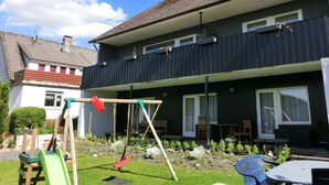 Ein zweigeschossiges Wohnhaus mit Balkon, Schaukel und einem Garten mit Tisch und Stühlen.