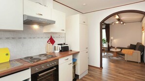 Eine moderne Küche mit weißen Schränken, einer Holz Arbeitsplatte und einem eingebauten Ofen. Es gibt einen Essbereich mit einer Couch und einem kleinen Tisch.