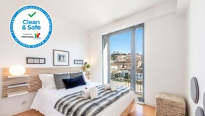 A modern hotel room with a large bed, a balcony with a city view, and a 'Clean & Safe' sign. - Martim Moniz Luxury Apartment (Lisboa)