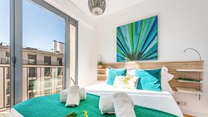 A modern bedroom with a large bed, green bedding, a view of buildings through a large window, and a colorful abstract painting on the wall. - Martim Moniz Luxury Apartment (Lisboa)