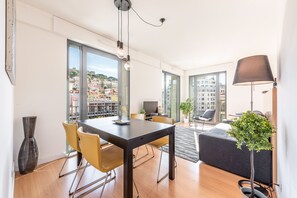 A modern living room with a dining area, large windows, and a view of the city.