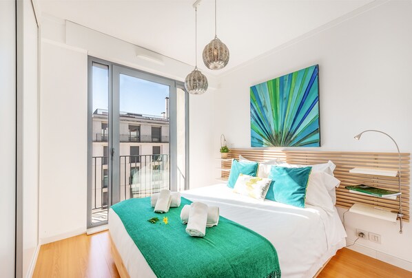 A modern bedroom with a large bed, a green throw blanket, and a view of the city through a sliding glass door.