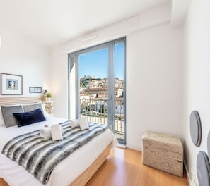 A modern hotel room with a large bed, a balcony with a city view, and a 'Clean & Safe' sign.