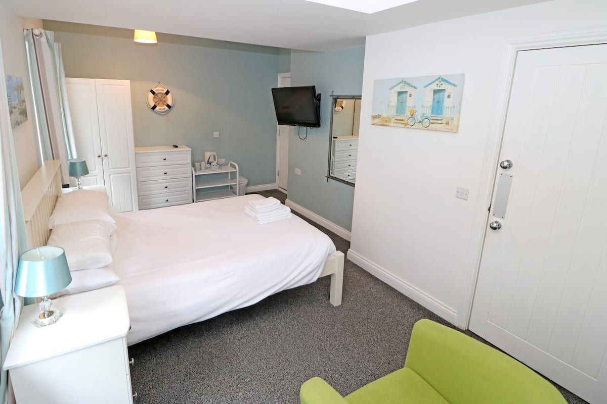 Un dormitorio con una cama, un aparador, una silla, un televisor y una puerta.