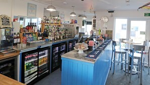 Una zona de bar con mostrador azul, estanterías llenas de botellas y un refrigerador con bebidas.