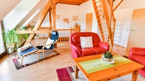 Een gezellige loftkamer met een houten plafond, een rode leren bank, een blauwe stoel en een houten tafel met een groene placemat.