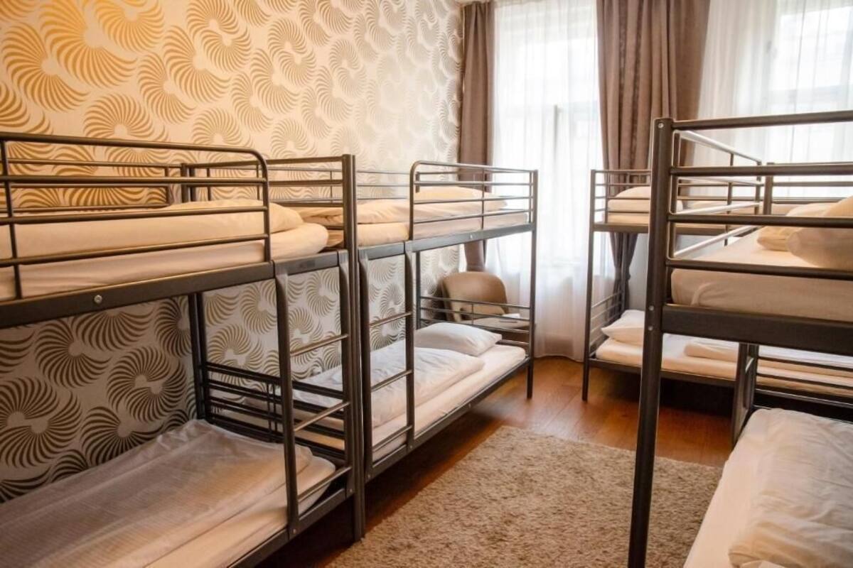 A room with bunk beds, a patterned wallpaper, and a window with curtains.
