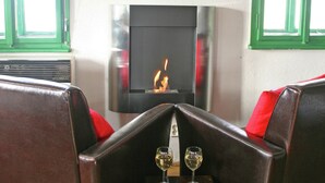 Una habitación con chimenea, asientos de cuero y dos copas de vino sobre una mesa.