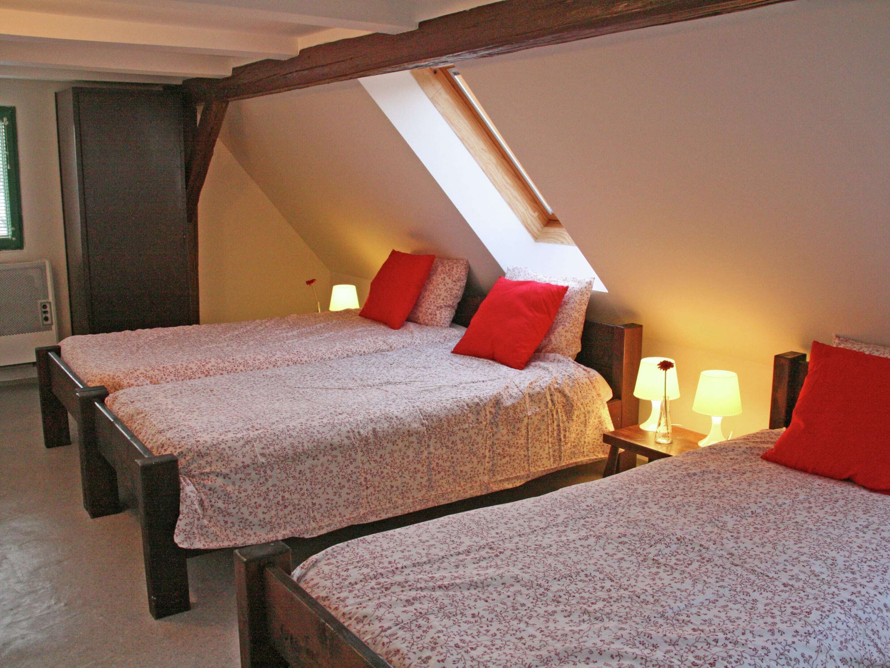 Un dormitorio con dos camas, cada una con cubrecama floral y almohadas rojas. Hay un tragaluz sobre las camas y una mesita de noche con lámpara entre ellas.