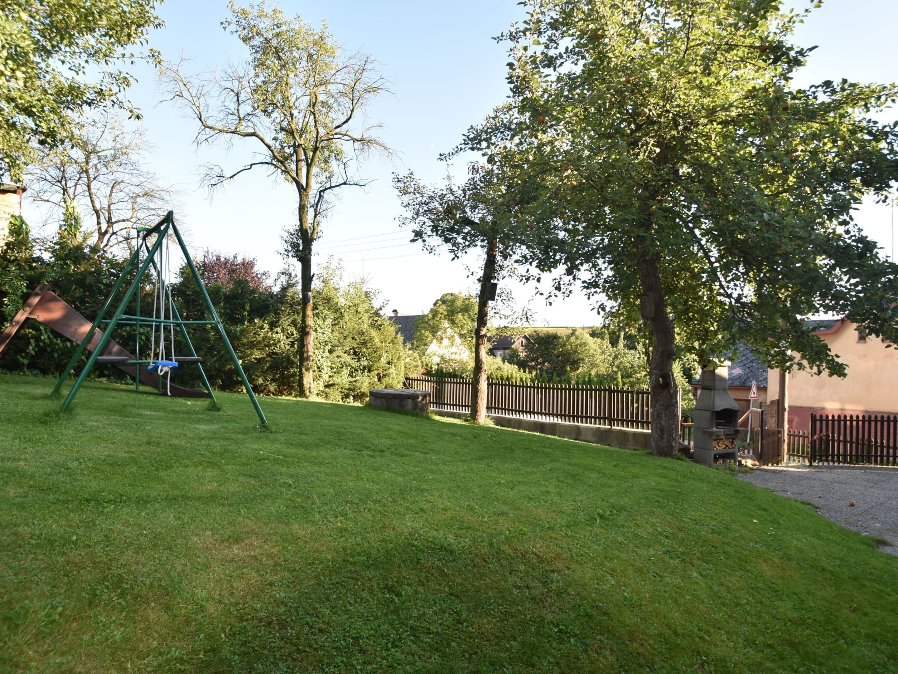 A grassy backyard with a swing set, a wooden fence, and trees.