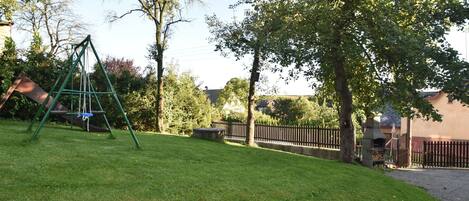 A grassy backyard with a swing set, a wooden fence, and trees.