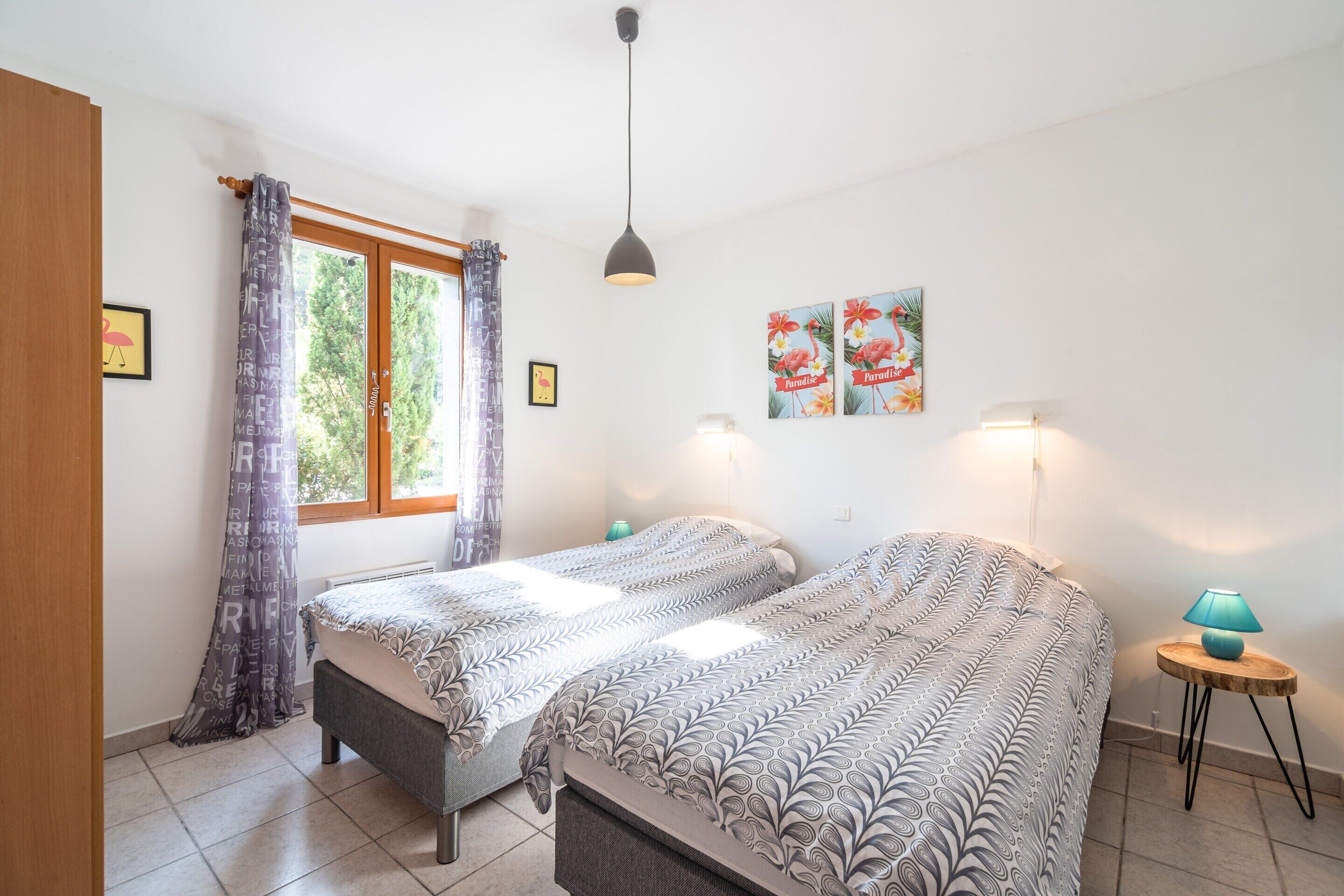 Ein Schlafzimmer mit zwei Betten, einem Fenster, einer Lampe und Wandbildern.