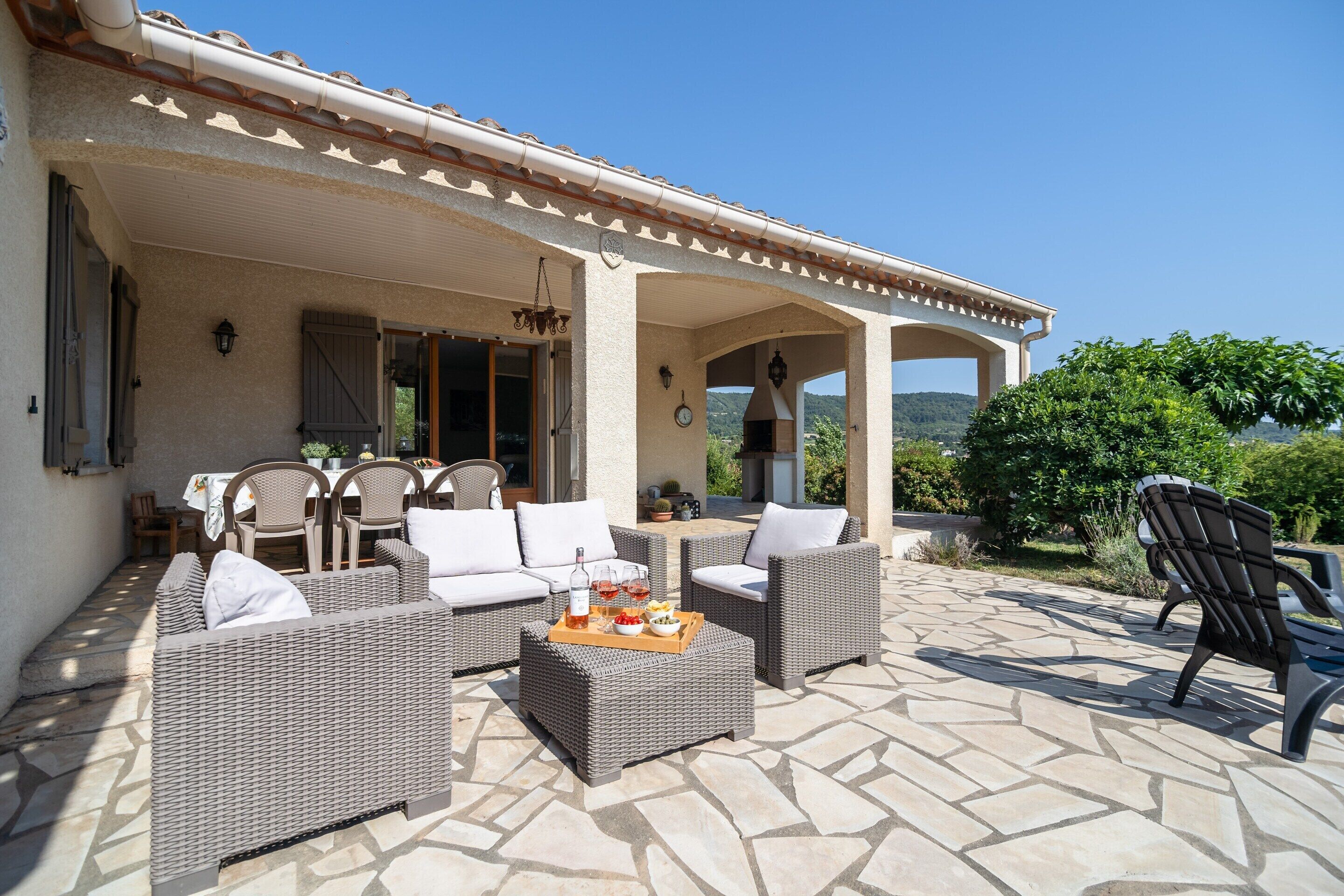 An outdoor patio with wicker furniture, a stone floor, and a view of the landscape.