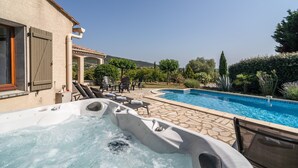 Un jacuzzi, mobiliario exterior y una piscina en un patio trasero.