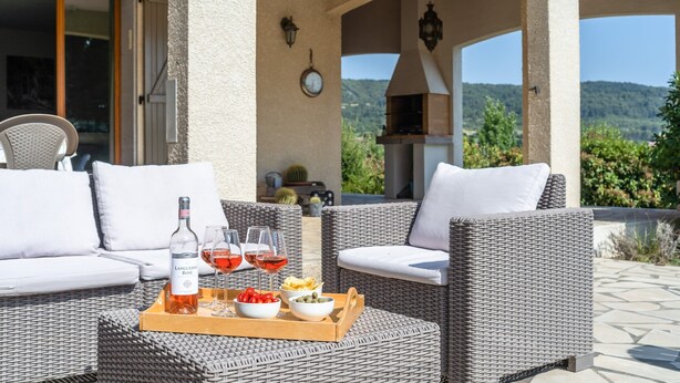Un patio con mobiliario de mimbre, una botella de vino, copas y fuentes de comida.