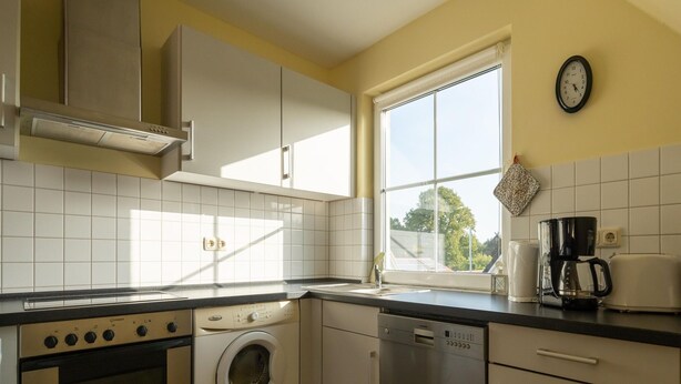 A kitchen with a washing machine, dishwasher, oven, and a coffee maker on the counter.