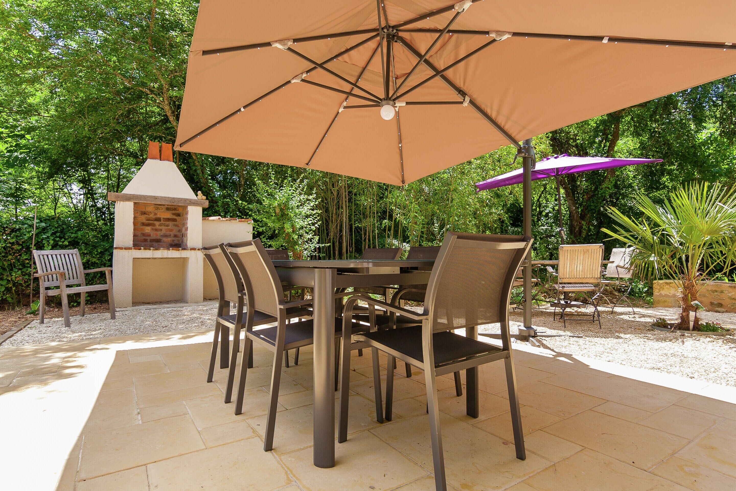 An outdoor patio with a brick fireplace, a table with chairs, and umbrellas providing shade.