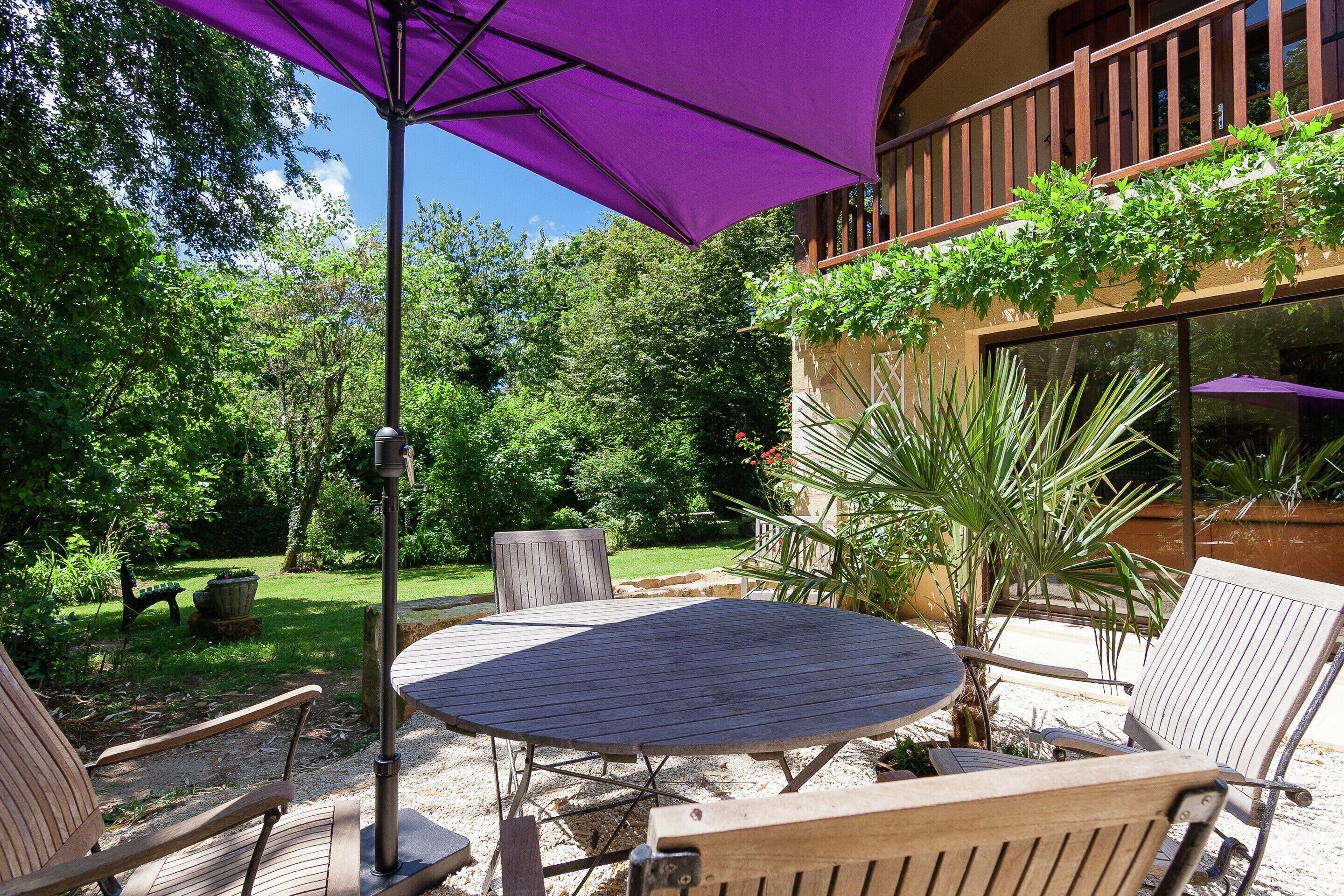 An outdoor patio with a round table, two chairs, and a purple umbrella.