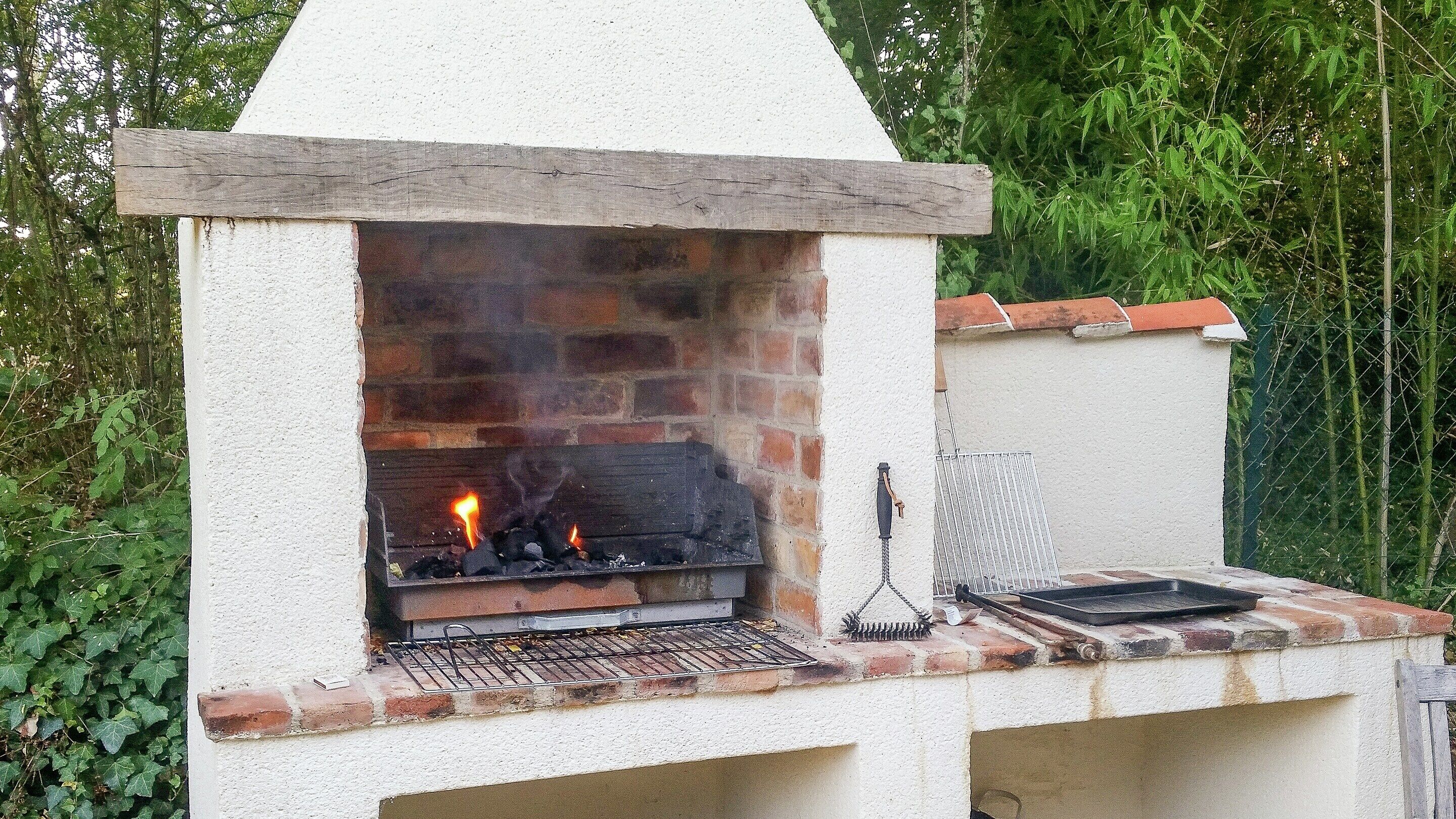 A brick-built outdoor grill with a chimney, a metal grill pan, and a metal rack on a white wall.