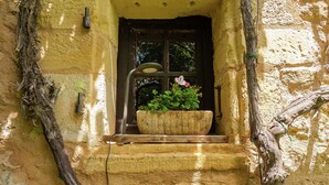 Um muro de pedra rústico com uma janela, um banco de madeira e um vaso com flores.