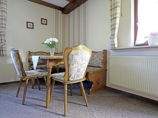 A dining area with a wooden table and four chairs, a vase with flowers, and a radiator. - Charming Apartment With Balcony, Garden, BBQ, Parking, Heating (Schmallenberg)