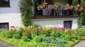A garden with various flowers and shrubs in front of a white building with a balcony. - Charming Apartment With Balcony, Garden, BBQ, Parking, Heating (Schmallenberg)