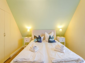A neatly made bed with white linens and a folded towel, two bedside lamps, and a wardrobe. - Vacation Home in Bastorf With Garden (Bastorf)