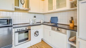 Une cuisine compacte dotée de meubles blancs, d’un four à micro-ondes, d’une machine à café, d’un grille-pain, d’un évier et d’un lave-vaisselle.
