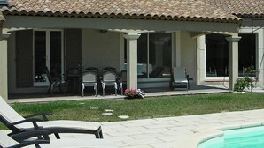 Ein Haus mit überdachter Terrasse, Sitzgelegenheit im Freien und einem Swimmingpool.