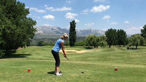 Ein Golfplatz mit blauem Himmel, Bäumen und Bergen in der Ferne.