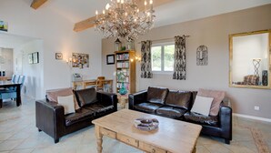A living room with a chandelier, leather sofas, a wooden coffee table, and a bookshelf. - Stylish Family Villa in Felines (Boutenac)
