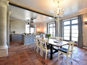 Ein geräumiger Essbereich mit großem Tisch und Stühlen, einer Chandelüster und einer Küche im Hintergrund.