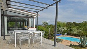A modern outdoor patio with a glass table and chairs, a pool, and lush greenery. - Villa in Malves Near Carcassonne Pool (Malves-en-Minervois)