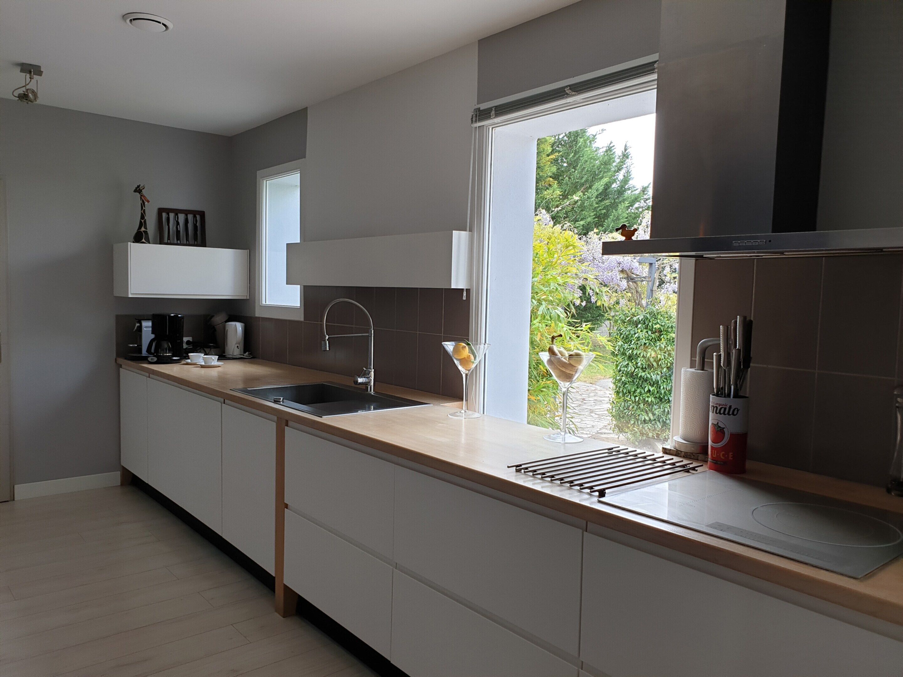 A modern kitchen with a large window, a built-in sink, and a countertop with a coffee maker.