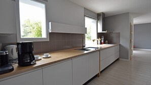 A modern kitchen with a wooden countertop, white cabinets, a coffee maker, and a window providing natural light. - Villa in Malves Near Carcassonne Pool (Malves-en-Minervois)
