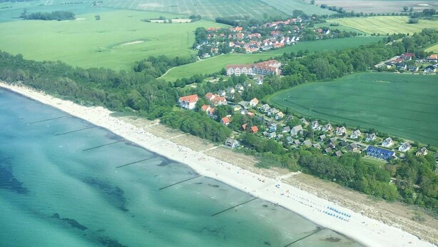 Luftaufnahme einer Küstenstadt mit Strand, grünen Feldern und Häusern.