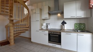Eine Küche mit weißen Schränken, einer Holztreppe, einer Kaffeemaschine und einer grünen Spritzschutzwand.