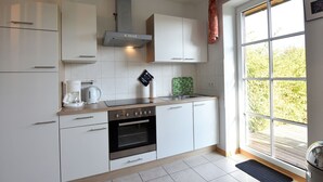 Eine moderne Küche mit weißen Schränken, einem Backofen, einer Kaffeemaschine und einem Fenster mit Blick auf Grünflächen.