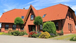 Ein rotes Backsteinhaus mit steilem Dach, zahlreichen Fenstern und einem gepflegten Garten mit verschiedenen Pflanzen und Blumen.