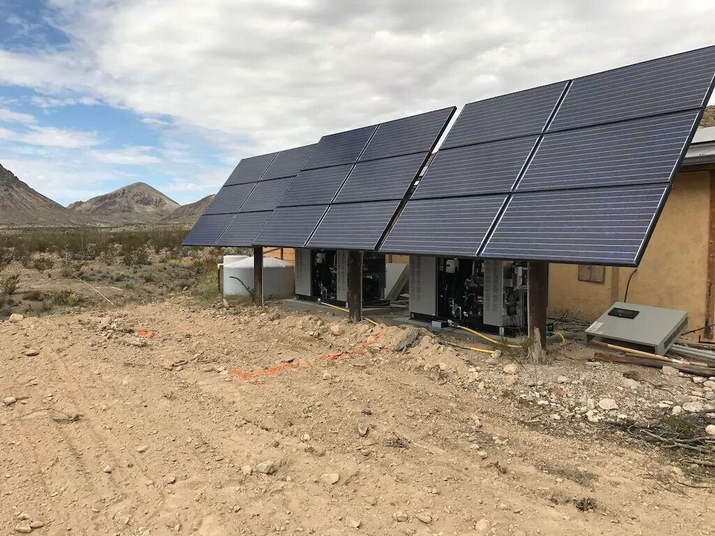 Ein Gebäude mit Solaranlage auf dem Dach, eine Wüstenlandschaft und Berge im Hintergrund.