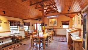 Un vaste espace dédié à la salle à manger, avec des tables et des chaises en bois, un haut plafond également en bois et des tapis à motifs sur le sol.