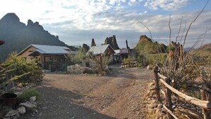 Un chalet rustique avec une allée en gravier, entouré d’un terrain rocailleux et d’une végétation clairsemée.