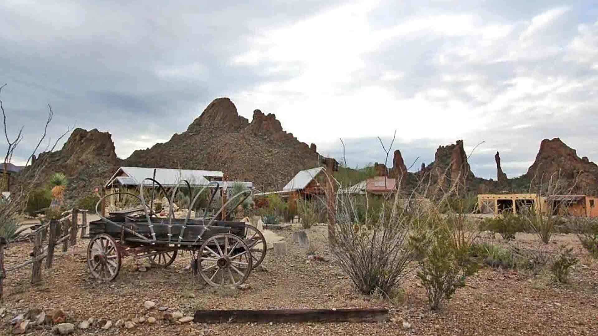 A rustic setting with a vintage carriage, rocky terrain, and sparse vegetation.