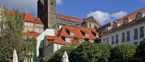 A courtyard with stone paving, outdoor seating, and a historic building with a tower.