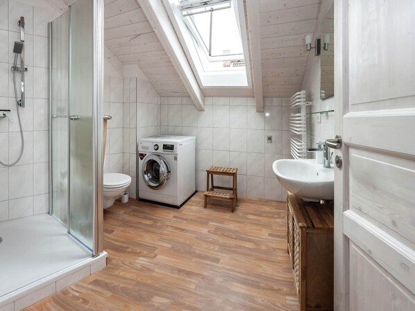 A modern bathroom with a skylight, a glass shower enclosure, a washing machine, and a wooden stool.