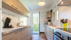 A modern kitchen with wooden cabinets, a coffee machine, a toaster, and a window with a view of greenery. - Lovely Country House With Private Pool (Vieussan)