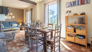 A dining area with a wooden table and chairs, a sofa, and a bookshelf with baskets. - Lovely Country House With Private Pool (Vieussan)